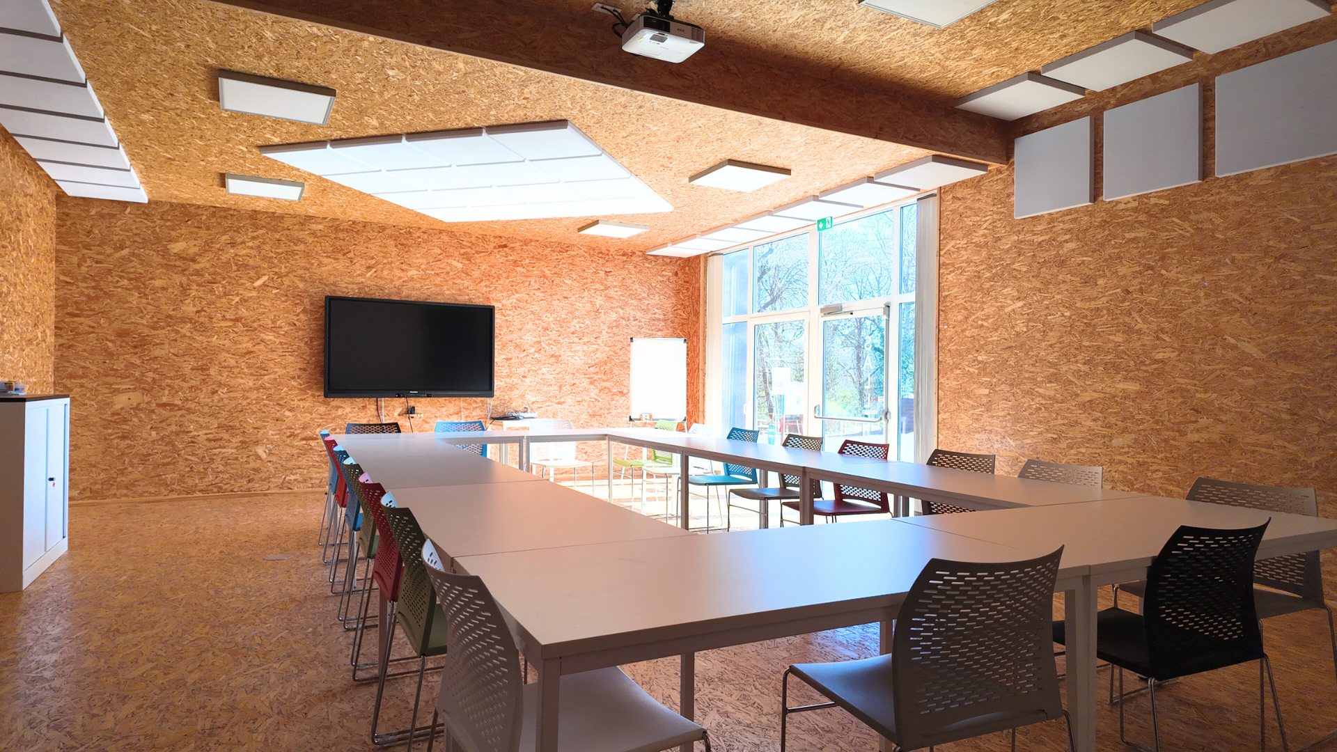 La Box : grande salle aux murs en bois OSB avec tables en U et écran tactile