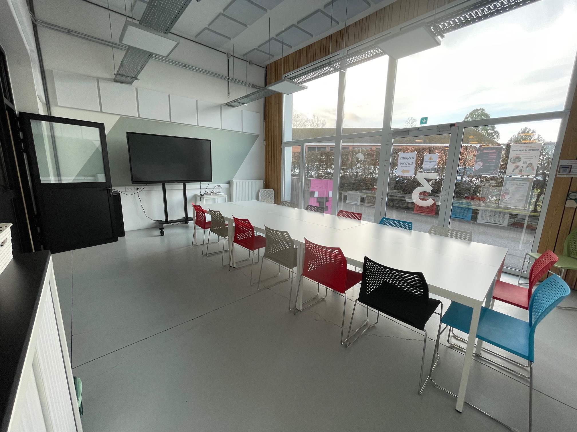 La Créative : salle lumineuse avec grandes baies vitrées, écran tactile et chaises colorées