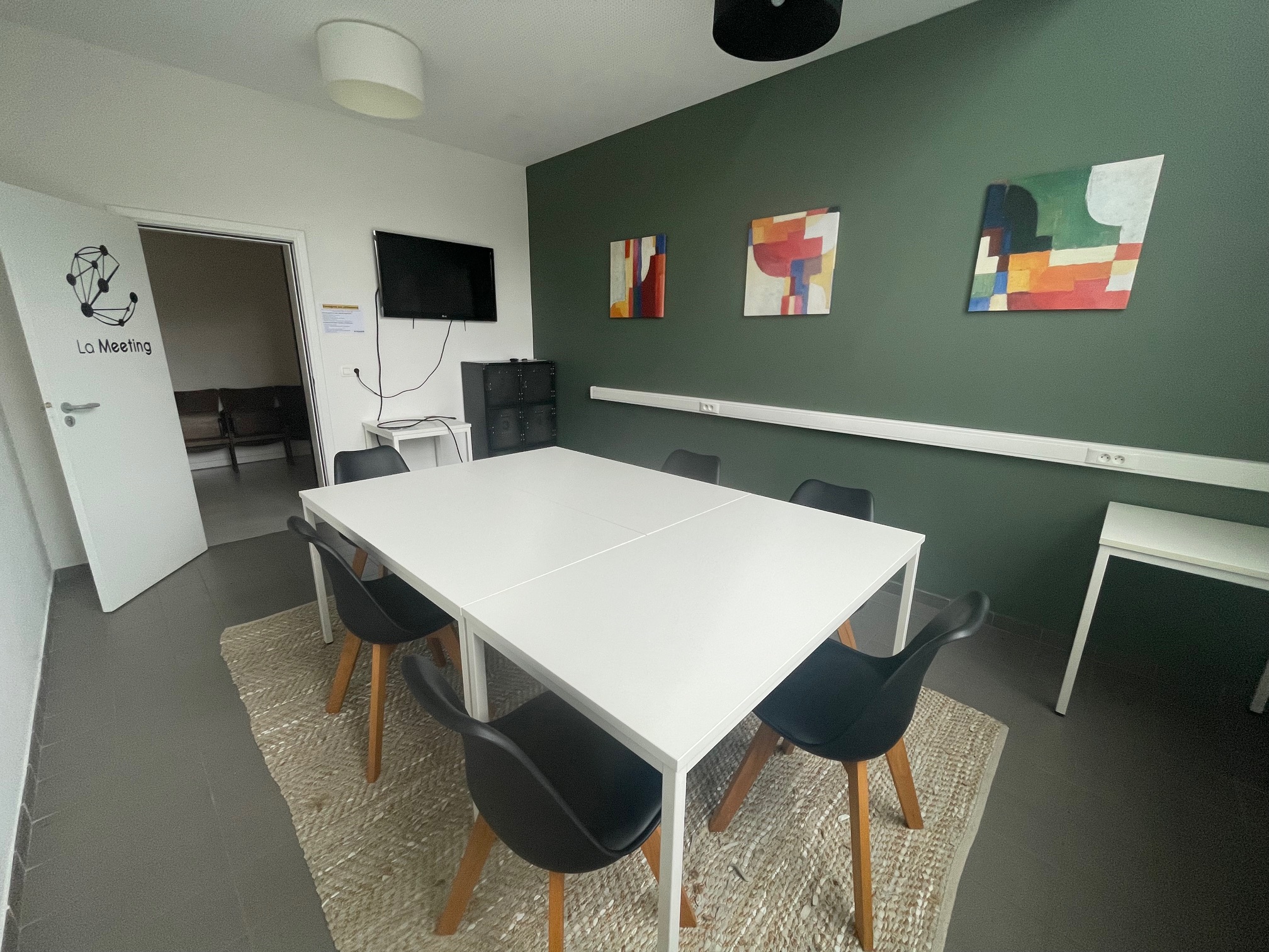 La Meeting : table blanche entourée de chaises devant un mur vert et un écran TV