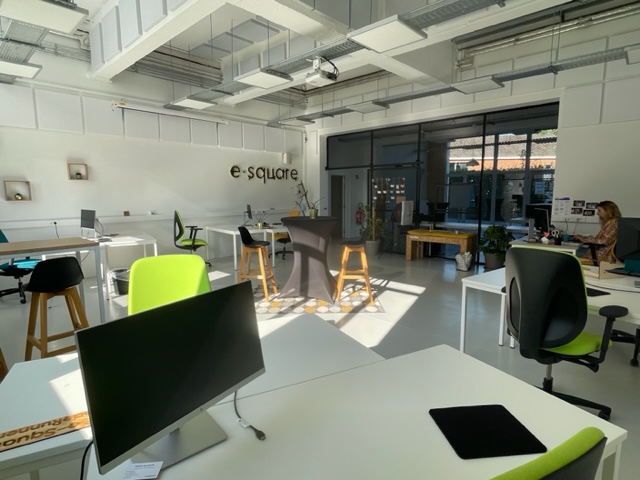 Le soleil du matin traverse la salle de coworking et éclaire la table haute centrale.
