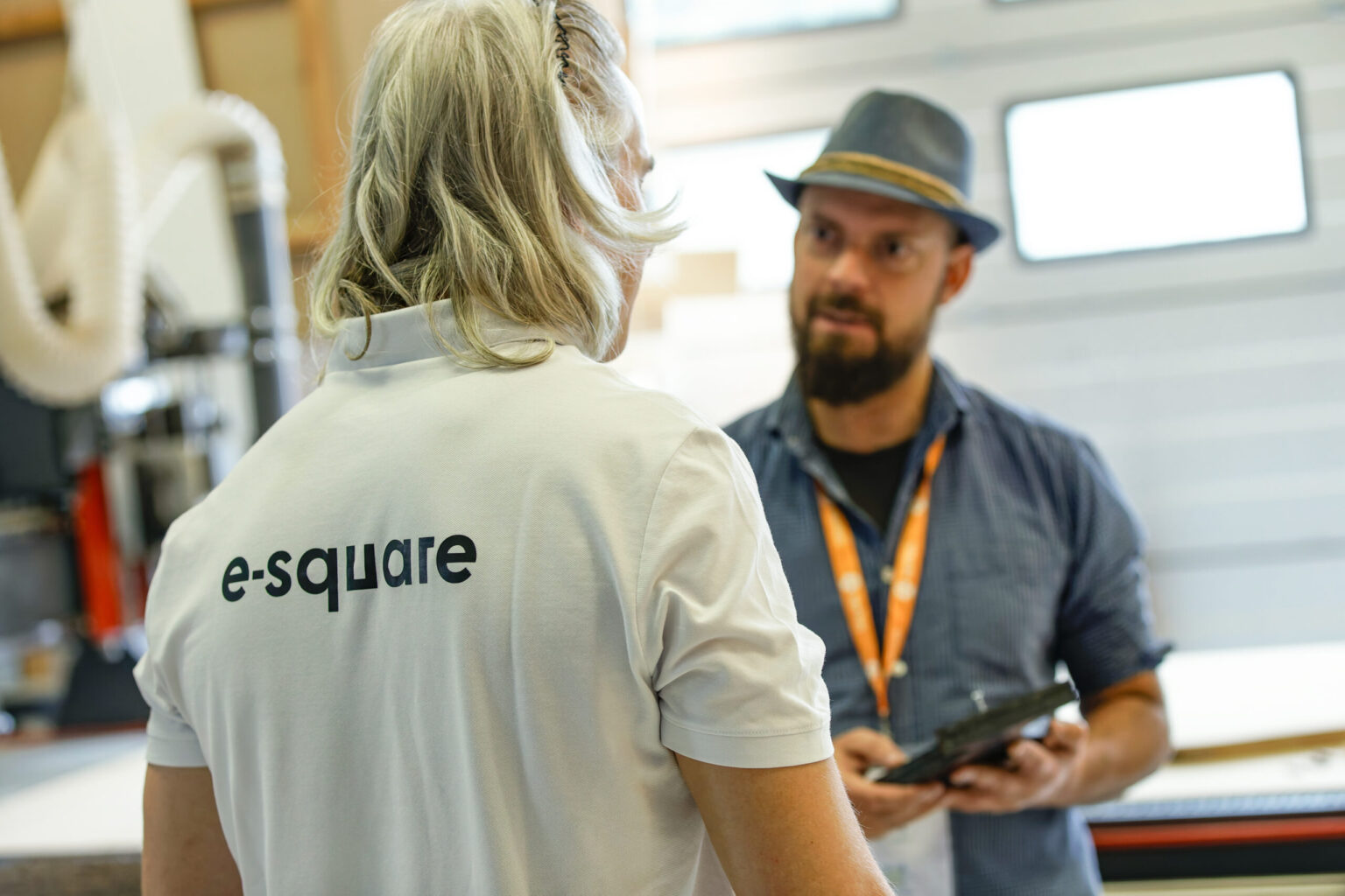 Un membre de l'équipe e-Square, en polo blanc, échange avec un participant devant la fraiseuse numérique.