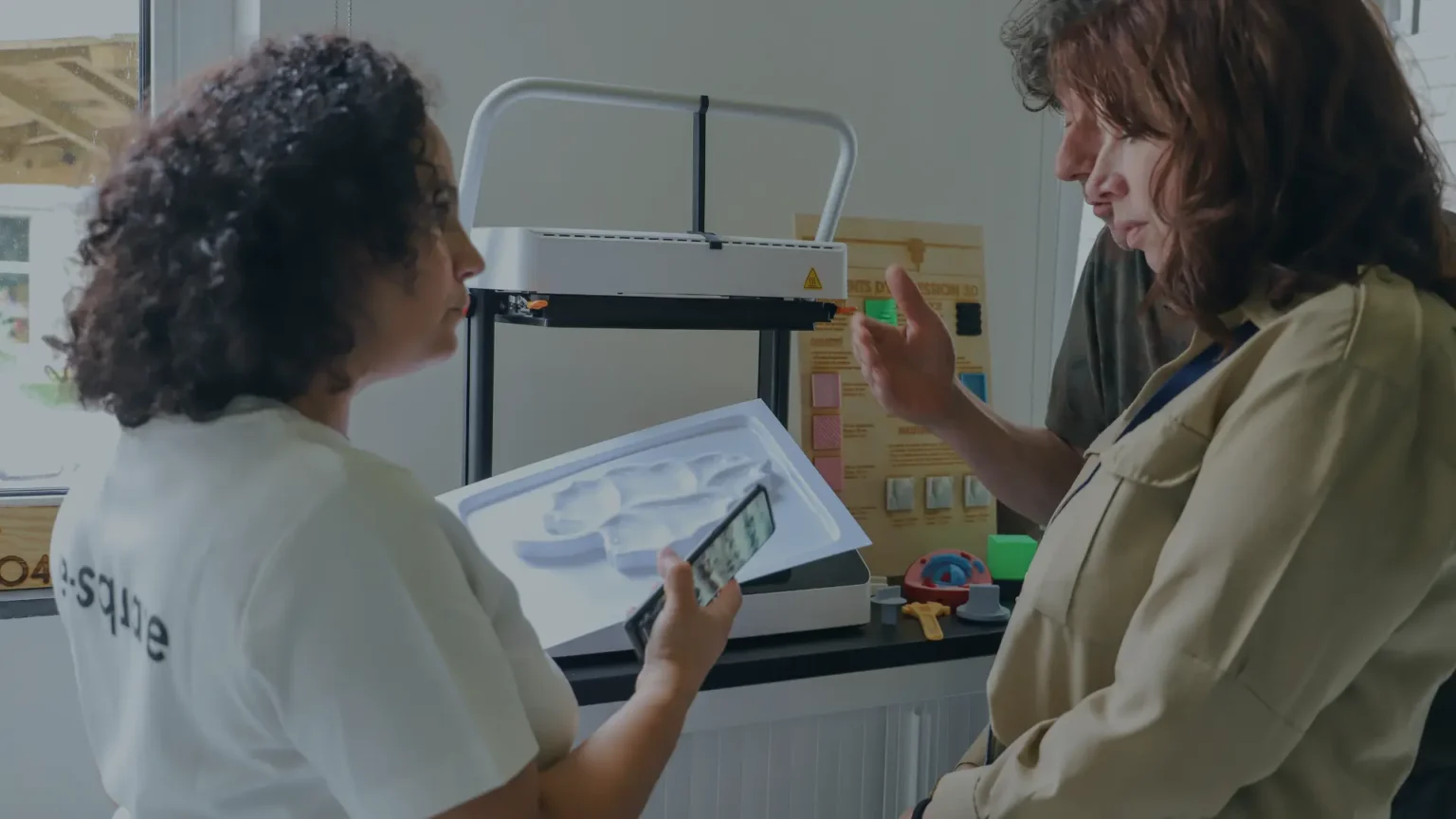 Une animatrice de l'e-Square et une visiteuse discutent d'une pièce thermoformée devant la machine.